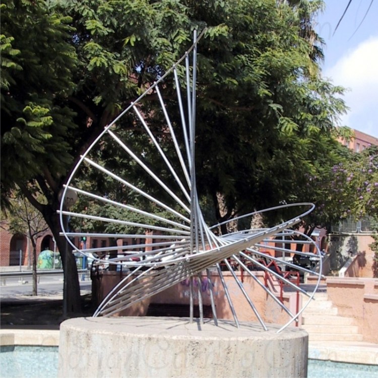 Escultura de acero circular en tres dimensiones sobre peana de cemento en medi ode un parque