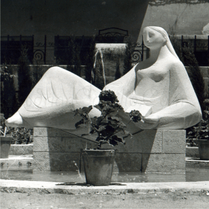 Figura de señora sobre piedra detras de una maceta